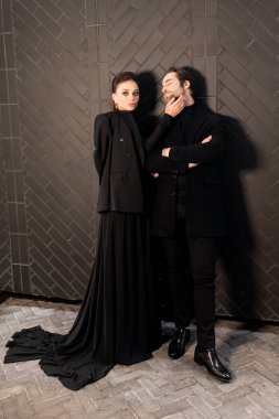 Siyahlar içinde dergi kapağı için fotoğraf çeken beyaz bir çift. Çekici sakallı genç kadın kameraya poz veriyor, manken konsepti.. 