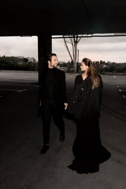 Şık takım elbiseli yakışıklı sakallı adamın portresi ve akşam vakti dışarıda yürüyen siyah elbiseli muhteşem kadın..