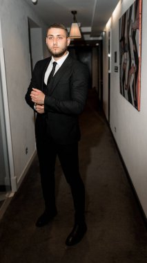 Koridorda duran siyah takım elbiseli ve beyaz gömlekli genç yakışıklı adam.