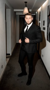 Koridorda duran siyah takım elbiseli ve beyaz gömlekli genç yakışıklı adam.