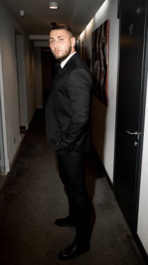 Koridorda duran siyah takım elbiseli ve beyaz gömlekli genç yakışıklı adam.