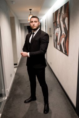 Koridorda duran siyah takım elbiseli ve beyaz gömlekli genç yakışıklı adam.