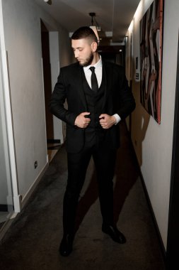 Koridorda duran siyah takım elbiseli ve beyaz gömlekli genç yakışıklı adam.