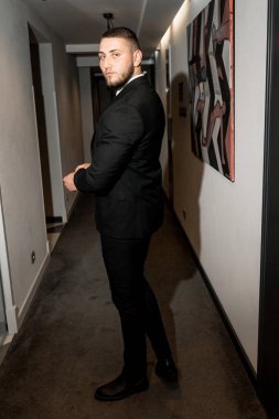 Koridorda duran siyah takım elbiseli ve beyaz gömlekli genç yakışıklı adam.