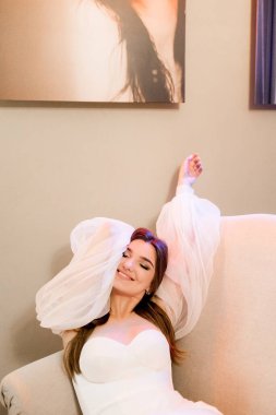 Kanepede poz veren beyaz elbiseli çekici bir kadının portresi.