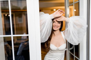 Pencerenin yanında beyaz elbiseli güzel bir kadın poz veriyor.