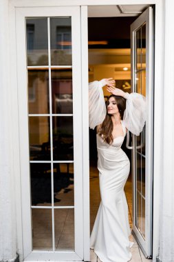 Pencerenin yanında beyaz elbiseli güzel bir kadın poz veriyor.