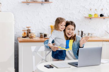 Güzel genç bir kadın ve Ukrayna bayraklarıyla evde dizüstü bilgisayar kullanan kızı.