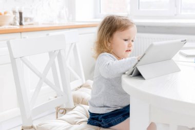 Bilgisayarlı küçük kız mutfaktaki masada oturuyor. 