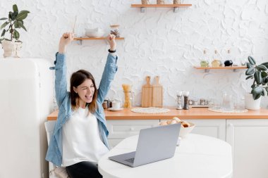 Mutfakta dizüstü bilgisayarı olan mutlu genç bir kadın.