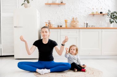 Genç anne ve kızı evde yoga egzersizleri yapıyorlar.