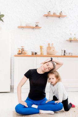 Genç anne ve kızı evde yoga egzersizleri yapıyorlar.