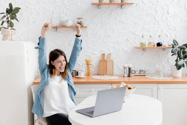 Mutfakta dizüstü bilgisayarı olan mutlu genç bir kadın.