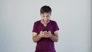 Süper heyecanlı erkek öğrenci. Beyaz adam kazanan teklifi kutluyor ya da akıllı telefondan ecommerce alışveriş teklifi alıyor. Heyecanlı erkek kazanan cep telefonuna bakarak başarıyı kutlayan bir uygulama kullanıyor, büyük testis gözlü.