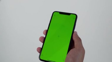 Arkadan çekilen kamera, elinde cep telefonu olan, elinde yeşil ekran, arkasında Krom Anahtar Yeşil Ekran İzleyen Akıllı Telefon olan bir adamın görüntüsünü kaydediyor.