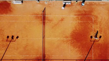 Tenis kortunun dron görüntüsü dikey üst görüş, oyuncu gölgesi siluet tenisçisinin sulu kırmızı kaplama üzerindeki görüntüsü