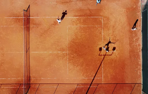 Tenis kortunun dron görüntüsü dikey üst görüş, oyuncu gölgesi siluet tenisçisinin sulu kırmızı kaplama üzerindeki görüntüsü