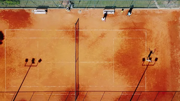Tenis kortunun dron görüntüsü dikey üst görüş, oyuncu gölgesi siluet tenisçisinin sulu kırmızı kaplama üzerindeki görüntüsü