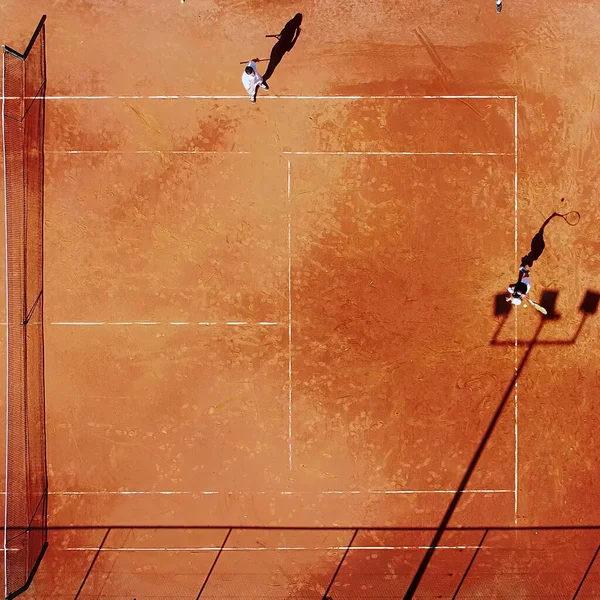 Tenis kortunun dron görüntüsü dikey üst görüş, oyuncu gölgesi siluet tenisçisinin sulu kırmızı kaplama üzerindeki görüntüsü