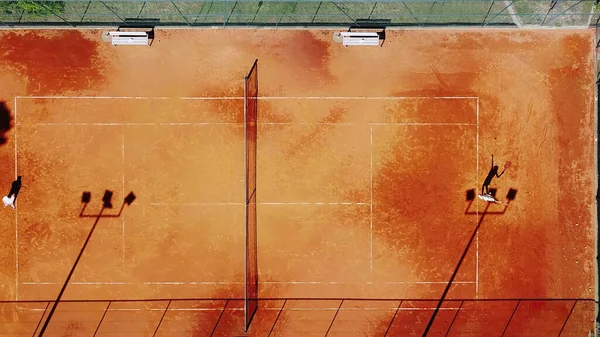 Tenis kortunun dron görüntüsü dikey üst görüş, oyuncu gölgesi siluet tenisçisinin sulu kırmızı kaplama üzerindeki görüntüsü