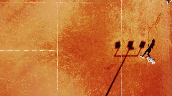 Tenis kortunun dron görüntüsü dikey üst görüş, oyuncu gölgesi siluet tenisçisinin sulu kırmızı kaplama üzerindeki görüntüsü