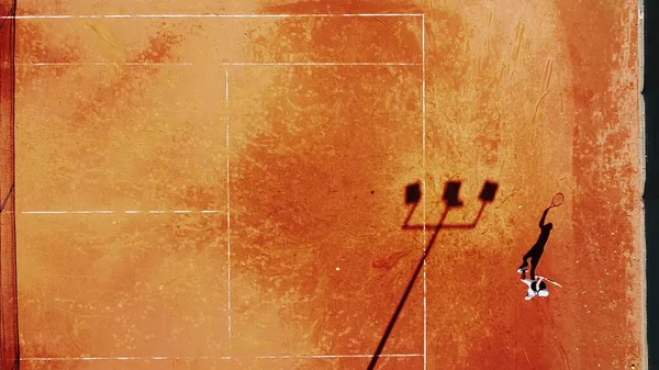 Tenis kortunun dron görüntüsü dikey üst görüş, oyuncu gölgesi siluet tenisçisinin sulu kırmızı kaplama üzerindeki görüntüsü