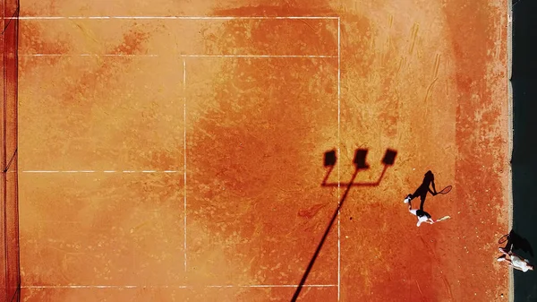 Tenis kortunun dron görüntüsü dikey üst görüş, oyuncu gölgesi siluet tenisçisinin sulu kırmızı kaplama üzerindeki görüntüsü