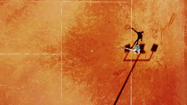 Tenis kortunun dron görüntüsü dikey üst görüş, oyuncu gölgesi siluet tenisçisinin sulu kırmızı kaplama üzerindeki görüntüsü