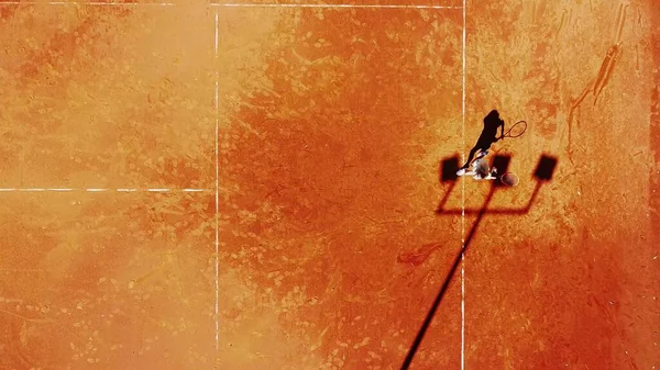 Tenis kortunun dron görüntüsü dikey üst görüş, oyuncu gölgesi siluet tenisçisinin sulu kırmızı kaplama üzerindeki görüntüsü