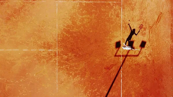 Tenis kortunun dron görüntüsü dikey üst görüş, oyuncu gölgesi siluet tenisçisinin sulu kırmızı kaplama üzerindeki görüntüsü