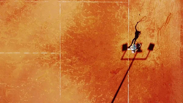 Tenis kortunun dron görüntüsü dikey üst görüş, oyuncu gölgesi siluet tenisçisinin sulu kırmızı kaplama üzerindeki görüntüsü