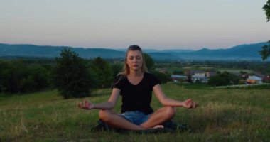 Kadın gün doğumunda çayırda yoga yapıyor. Genç ruhani kız nilüfer çiçeğiyle meditasyon yapar. Doğa poz verir, ağır çekimde. Zindelik kavramı, sağlıklı yaşam tarzı