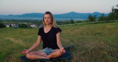 Kadın gün doğumunda çayırda yoga yapıyor. Genç ruhani kız nilüfer çiçeğiyle meditasyon yapar. Doğa poz verir, ağır çekimde. Zindelik kavramı, sağlıklı yaşam tarzı