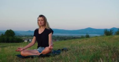 Kadın gün doğumunda çayırda yoga yapıyor. Genç ruhani kız nilüfer çiçeğiyle meditasyon yapar. Doğa poz verir, ağır çekimde. Zindelik kavramı, sağlıklı yaşam tarzı
