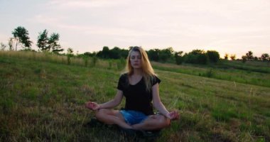 Kadın gün doğumunda çayırda yoga yapıyor. Genç ruhani kız nilüfer çiçeğiyle meditasyon yapar. Doğa poz verir, ağır çekimde. Zindelik kavramı, sağlıklı yaşam tarzı