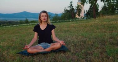 Kadın gün doğumunda çayırda yoga yapıyor. Genç ruhani kız nilüfer çiçeğiyle meditasyon yapar. Doğa poz verir, ağır çekimde. Zindelik kavramı, sağlıklı yaşam tarzı
