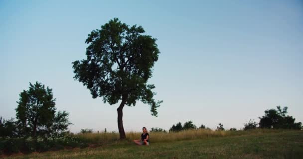 女人在日出时在草地上练习瑜伽 年轻的灵性女孩在荷花中沉思 把大自然置于户外 慢动作 健康生活方式的概念 — 图库视频影像