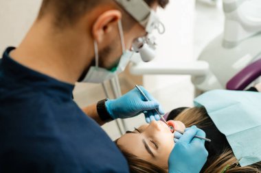 Doktor dişçi bir hastanın dişlerini mikroskop altında tedavi eder.