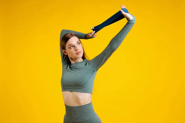 Sports girl with a rubber band for fitness on a yellow background. High quality photo