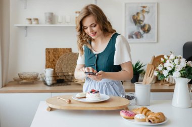 Güzel kız pastacı mutfakta bir pastanın fotoğrafını çekiyor. Yüksek kalite fotoğraf