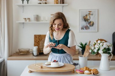 Güzel kız pastacı mutfakta bir pastanın fotoğrafını çekiyor. Yüksek kalite fotoğraf