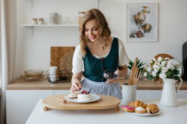 Beautiful girl adds a berry to the cake in the kitchen. High quality photo