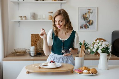 Beautiful girl adds a berry to the cake in the kitchen. High quality photo