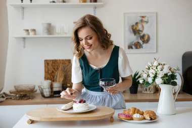 Beautiful girl adds a berry to the cake in the kitchen. High quality photo