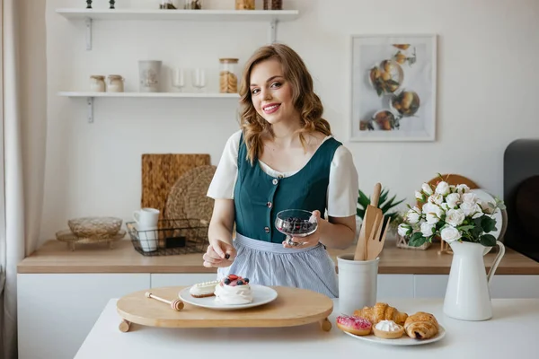 Beautiful girl adds a berry to the cake in the kitchen. High quality photo