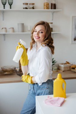 Beautiful girl in yellow gloves holding a cleaning spray in the kitchen. High quality photo