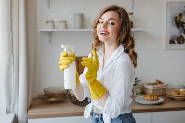 Beautiful girl in yellow gloves holding a cleaning spray in the kitchen. High quality photo