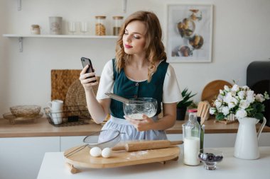 Beautiful girl holding a smartphone in her hand while cooking. High quality photo