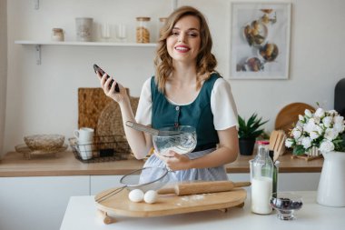 Beautiful girl holding a smartphone in her hand while cooking. High quality photo