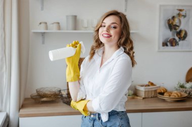 A girl in yellow gloves holds a cleaning spray on the background of the kitchen. High quality photo